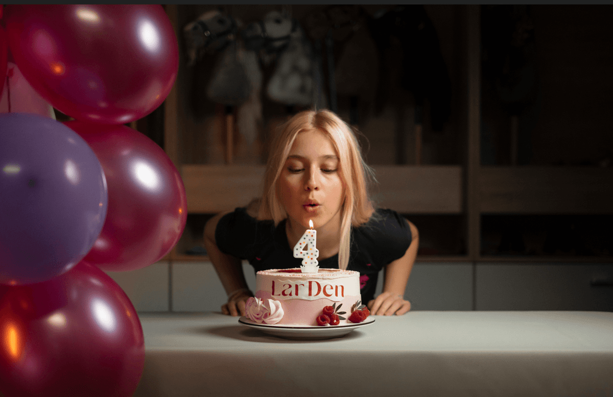 Lara soufflant une bougie en forme de chiffre quatre sur un gâteau d’anniversaire LarDen près de ballons colorés