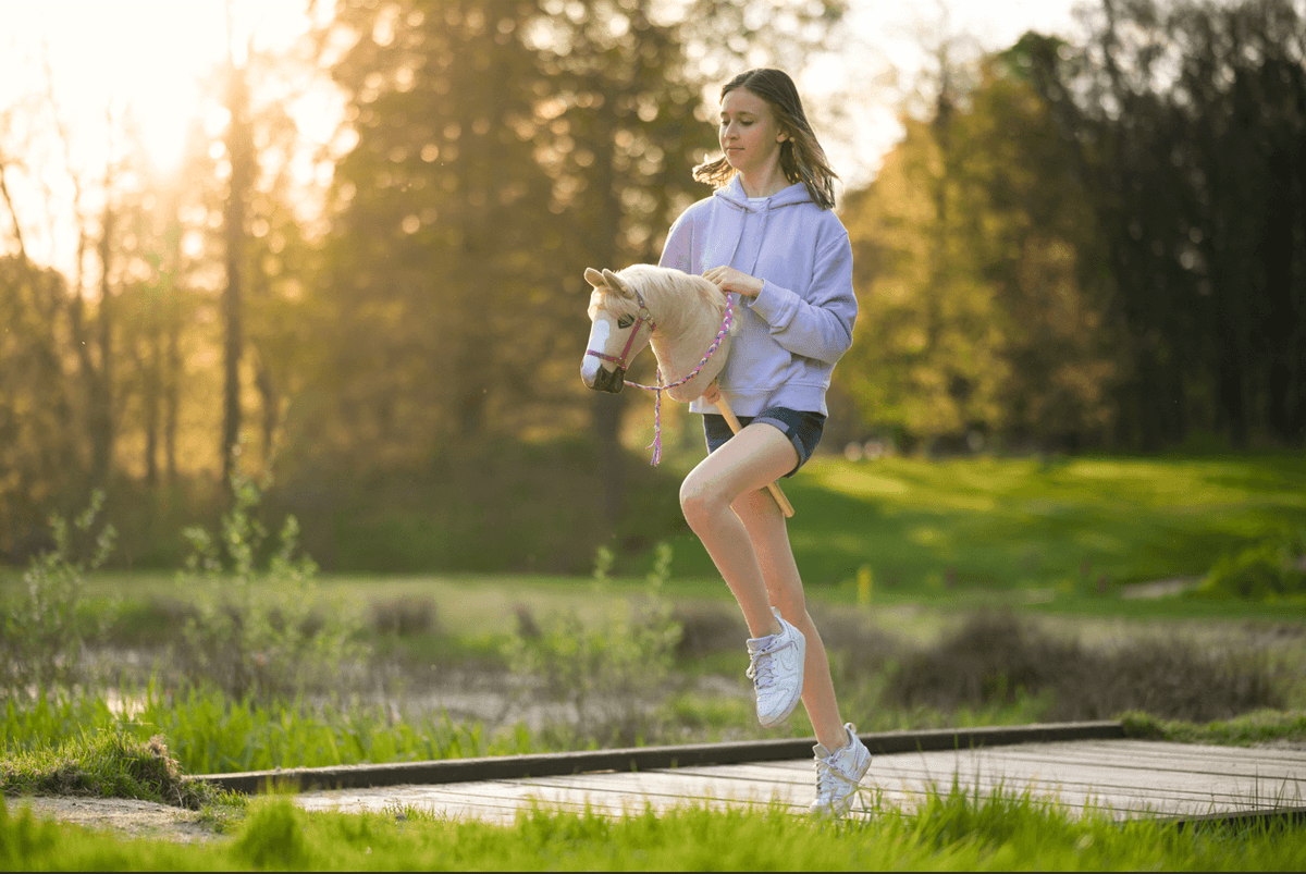 Fille pratiquant le Hobby Horsing en extérieur avec un Hobby Horse blanc au coucher du soleil