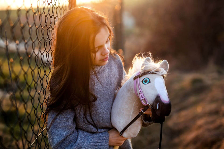 Young girl holding a white Hobby Horse with a pink bridle in warm sunset light