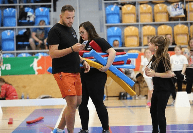 Denny préparant des obstacles colorés pour Hobby Horse avec un jeune participant au Hobby Horsing dans une salle de sport