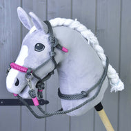 Un Hobby Horse gris et blanc en peluche avec crinière tressée et yeux noirs présente l’ensemble de corde gris (taille M) de Hobby Horse LarDen devant des panneaux en bois, mettant en valeur un équipement d’équitation artisanal unique.