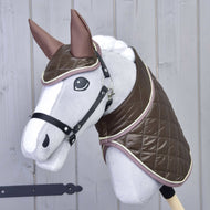 Ensemble Thermo Chocolat de Hobby Horse LarDen, sur un Hobby Horse gris aux grands yeux, habillé d’une couverture matelassée marron brillante et d’un bonnet d’oreilles assorti, monté sur un bâton devant un mur en bois clair.