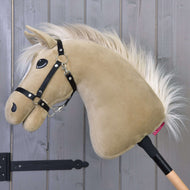 Hobby Horse Dancing Lady avec licol noir de Hobby Horse LarDen avec tête de jument Pur-sang anglais en peluche, robe beige et crinière blanche sur un bâton en bois, présentée devant un mur de panneaux en bois gris.
