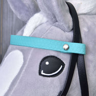 Close-up of a gray plush Hobby Horse LarDen horse's head wearing a turquoise Complete bridle without noseband. Features include a black rein, white ear, white face markings, and a cartoon-style eye with black outline and white highlight.