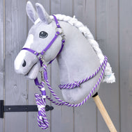 Ensemble Départ Violet (licol + cordelette + longe + rênes) de Hobby Horse LarDen, présenté sur un Hobby Horse en peluche avec tête grise, crinière blanche et liste blanche, monté sur un bâton en bois devant un mur en bois gris.