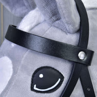 Gros plan sur le visage d’un cheval en peluche gris avec la Bride complète noire en similicuir de Hobby Horse LarDen, montrant un œil brodé noir et blanc et un tissu doux texturé avec coutures visibles.