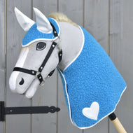 The Hobby Horse LarDen "Set Mystery" features a gray horse with a blue textured blanket-like cover, white ears, a white heart on its side, black bridle, thick white mane, and is mounted on a stick against a wooden background.