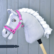 Licol rose avec fourrure de Hobby Horse LarDen présenté sur un Hobby Horse gris avec crinière blanche en fil, marques blanches sur le visage et monté sur un bâton en bois devant un fond en bois gris.