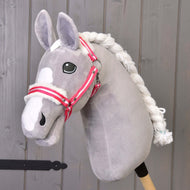 Licol rayé rouge avec fourrure de Hobby Horse LarDen sur un Hobby Horse gris en peluche avec crinière blanche et licol à rayures rouges, monté sur un bâton en bois devant un mur en bois gris.