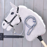 Hobby Horse - Corde de meneur tricotée Cremo-Bleu de Hobby Horse LarDen, en gris, avec bride noire et longe tricotée bleue et blanche, suspendu sur un mur en bois près d’une charnière métallique noire.