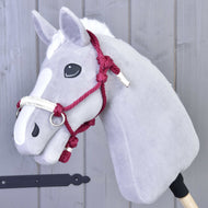 Licou en corde Czi-Czi de Hobby Horse LarDen, Hobby Horse en peluche gris avec liste blanche, yeux noirs en bouton et cet accessoire, monté sur un bâton en bois devant un mur en bois gris.