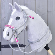 The Hobby Horse LarDen Rope set Rosie, a gray plush hobby horse with a white blaze, black eyes, and a pink and gray bridle with reins on a wooden stick, is shown in front of a light gray wooden wall.