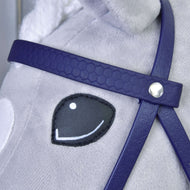 Gros plan sur le visage d’un cheval en peluche avec œil noir et blanc cousu, portant la Bride complète avec muserolle Violet foncé de Hobby Horse LarDen ; la bride présente un détail de bouton argenté et le pelage du cheval est gris clair.