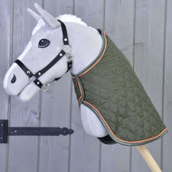 Hobby Horse gris en peluche sur bâton, avec la Couverture Sport verte à bordure orange de Hobby Horse LarDen et un licol noir, devant un mur en bois avec une charnière en fer noir.