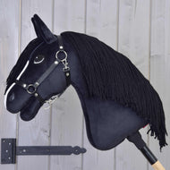 The Hobby Horse LarDen Freya with Black Halter, featuring a white facial stripe and black yarn mane on a wooden stick, is set against a light gray wooden wall—perfect for any family horse enthusiast.