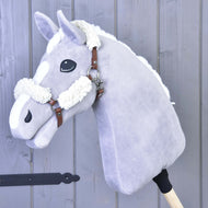 The Hobby Horse LarDen Brown halter with complete fur – leatherette is a plush, light gray hobby horse featuring a white mane and markings, set on a wooden stick and photographed against a gray wooden panel background.