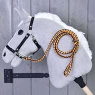 Hobby Horse - Corde de meneur tricotée Pomello de Hobby Horse LarDen, Hobby Horse en peluche gris avec crinière blanche, bride noire et longe tricotée orange et noire avec mousqueton, monté sur un mur en bois.