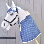 Ensemble Manchester Prune de Hobby Horse LarDen avec Hobby Horse en peluche au visage blanc, bride noire et couverture matelassée bleue, ainsi qu’un bonnet d’oreilles assorti, posé devant un mur en bois clair.