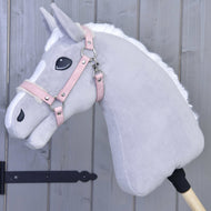 Licol avec fourrure - similicuir Mulberry de Hobby Horse LarDen, Hobby Horse en peluche gris clair avec crinière blanche, bride en similicuir rose et détails brodés, monté sur un bâton en bois devant un mur en bois gris.