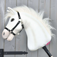 Hobby Horse Nexus avec licol noir de Hobby Horse LarDen, un cheval de sport blanc en peluche avec crinière duveteuse, grand œil bouton et licol noir, parfait pour tout passionné. Photografié devant un mur en bois gris.