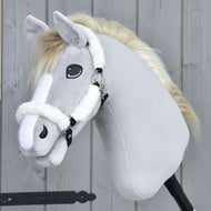 Hobby Horse LarDen Licol en fourrure Teddy Classique, un Hobby Horse en peluche avec fourrure gris clair, crinière blanche, marques faciales blanches et licol blanc, monté sur un bâton devant un fond en bois.