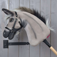 The Hobby Horse LarDen "Hobby Horse Donkey Olin with Black Halter" features a gray plush donkey head with a dark mane, a black halter, reins, and a silver ring near its mouth on a wooden stick, set against a gray wall.