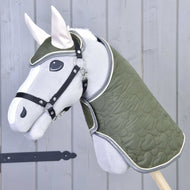 Ensemble Olivetti de Hobby Horse LarDen avec Hobby Horse gris, couverture matelassée verte et bride, licol noir, oreilles blanches et accessoires élégants, présenté devant un mur en bois gris clair.