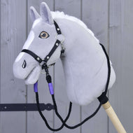 The Hobby Horse LarDen Reins Basic Lila, handmade from polypropylene rope, is shown with a gray plush hobby horse featuring a white mane and black bridle, mounted on a wooden stick before a gray wooden fence.