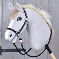The Hobby Horse LarDen plush hobby horse features a light gray face, black bridle, white mane, and is mounted on a wooden stick. It comes with handmade "Reins Emblem CZ" adorned with a blue, white, and red charm.