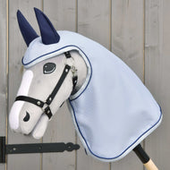 Imperméable Luméa de Hobby Horse LarDen sur un Hobby Horse gris en peluche monté sur bâton, avec une bride noire, un imperméable bleu et des protège-oreilles bleu marine, présenté devant un fond en bois clair.