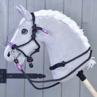 Ensemble de corde Princesse de Hobby Horse LarDen sur un Hobby Horse gris avec crinière blanche, licol détaillé et rênes noirs, plus accents roses et turquoise, monté sur un bâton en bois devant un fond en planches grises.