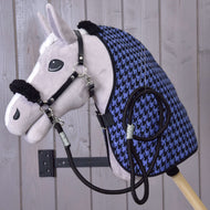 Ensemble Harmonie Bleu de Hobby Horse LarDen, hobby horse en peluche avec licol noir, rênes et couverture d’écurie pied-de-poule bleu et noir, fixé au mur sur fond de planches en bois clair.