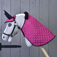 Hobby Horse en peluche de Hobby Horse LarDen sur un bâton en bois, avec visage blanc, bride noire, et portant la couverture et le bonnet d'oreilles Ensemble Thermo Rose devant un mur gris, une charmante décoration équestre.