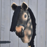 Hobby Horse Stormy avec licol noir de Hobby Horse LarDen, étalon hanovrien gris pommelé réaliste avec crinière en fil noir et tête en peluche marron montée sur un bâton, présenté devant un mur en bois gris clair.