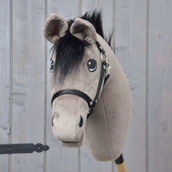 Hobby Horse Thor avec licol noir de Hobby Horse LarDen, avec tête grise douce, crinière noire et harnais sur un bâton en bois, sur fond de panneaux en bois clair.