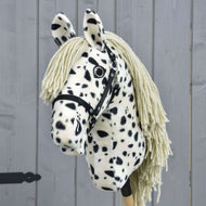 Hobby Horse Lord Valentine avec licol noir de Hobby Horse LarDen, avec robe tachetée noire et blanche, crinière en fil et licol noir, présenté sur un fond en bois gris.