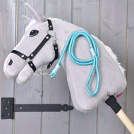 Hobby Horse - rayures corde Atlantis de Hobby Horse LarDen avec tête grise en peluche, bride noire et laisse en corde bleue, montée sur un bâton en bois et présentée devant des planches de bois verticales.