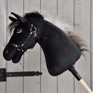 Hobby Horse Bond avec licol noir de Hobby Horse LarDen, un Hobby Horse noir en peluche avec crinière blanche, licol noir et rênes sur un bâton en bois, présenté devant un mur en bois clair, parfait pour tous les fans de Hobby Horse Bond.