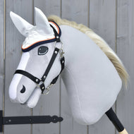Bonnet d'oreilles Speedy de Hobby Horse LarDen sur un Hobby Horse gris réaliste avec bride noire, crinière blanche et bonnet d'oreilles blanc anti-mouches, monté sur un bâton en bois devant un mur en bois gris clair.
