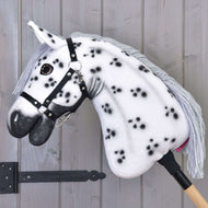 The Hobby Horse LarDen 'Hobby Horse Chantal with Black Halter' features a white coat with black spots, gray yarn mane, black halter, and is mounted on a wooden stick against a light gray wooden wall.