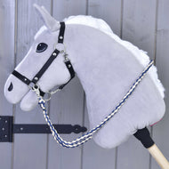 The Hobby Horse LarDen Reins Cremo/Blue is a plush gray hobby horse with a white mane, black bridle, handmade reins, silver hardware, and a blue-and-white braided lead rope on a wooden stick, shown against a gray wooden wall.