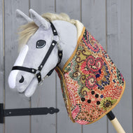 Hobby Horse LarDen « Blanket Jungle », hobby horse en peluche avec tête grise, bride noire et corps recouvert d'une couverture colorée — idéal pour le jeu imaginatif ou l'entraînement précoce du cheval — présenté sur fond de panneaux en bois.