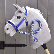 Ensemble Essentiel Bleu de Hobby Horse LarDen, sur un Hobby Horse en peluche gris avec crinière blanche, licol bleu bordé de fourrure et rêne en corde bleue et blanche sur un bâton en bois, devant une clôture en bois grise.