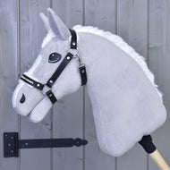 A gray hobby horse with a white mane and black bridle is mounted on a wooden stick, featuring the Hobby Horse LarDen Halter with fur - leatherette Espresso, positioned in front of a light gray wooden wall with a black hinge visible to the left.