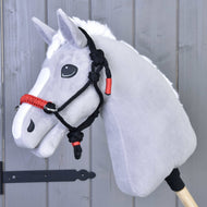 Licou en corde Spark de Hobby Horse LarDen sur un cheval jouet Hobby Horse gris avec crinière blanche et licou en corde noir et rouge, monté sur un bâton en bois devant un mur en bois gris.