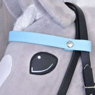 Gros plan sur le visage d’un cheval-jouet gris en peluche avec œil noir cousu, oreille blanche et Bride complète sans muserolle Bleu clair de Hobby Horse LarDen, avec sangle bleu clair, bouton argenté et rênes noires amovibles.
