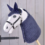 Ensemble Étoile Bleue de Manchester de Hobby Horse LarDen avec Hobby Horse gris, bride et rênes noires, ainsi qu’une couverture matelassée bleu marine et un bonnet à bordure blanche, présenté sur un bâton en bois sur fond de panneaux en bois clair.