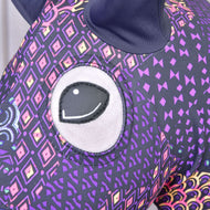 Gros plan sur la Combinaison de protection Hobby Horse Mandala (Lycra) de Hobby Horse LarDen montrant son grand œil brodé et son tissu violet aux motifs géométriques et losanges colorés ; une oreille foncée apparaît en haut.