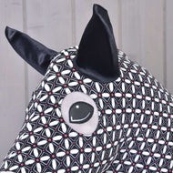Gros plan sur la Combinaison de protection DeLuxe pour Hobby Horse (Lycra) de Hobby Horse LarDen, montrant son tissu en lycra lavable à motif géométrique noir et blanc, ses grandes oreilles noires et son œil cousu sur un fond en bois clair.