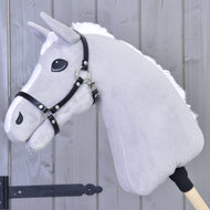 Hobby Horse en peluche grise de Hobby Horse LarDen, avec crinière blanche et Licol - similicuir noir, monté sur un bâton en bois devant un fond en panneaux de bois.